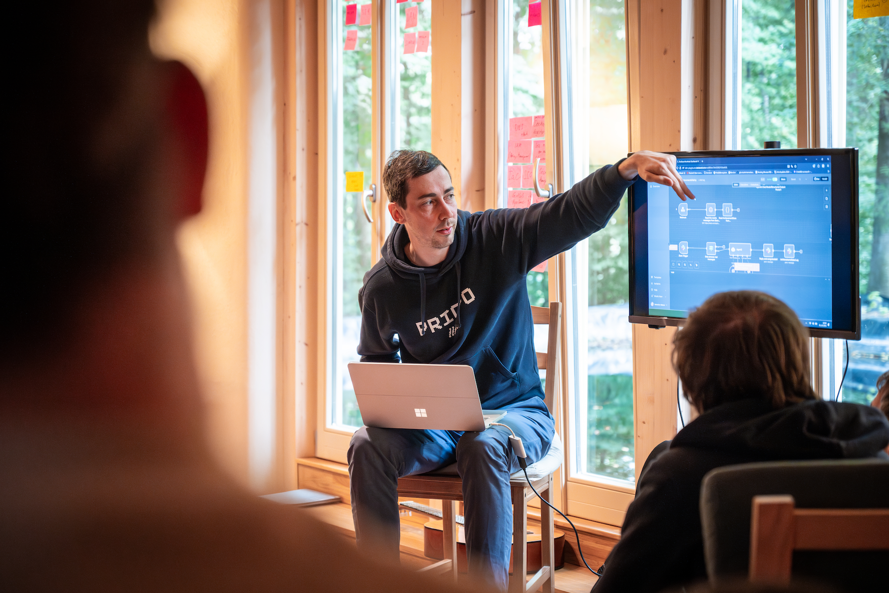 Ein DevBoost-Kollege sitzt mit Laptop auf einem Stuhl und erklärt die Workshop-Ergebnisse, während er auf ein Diagramm auf dem Bildschirm zeigt.